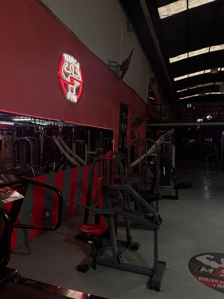 Pared roja con el neón de la marca y máquinas de musculación
